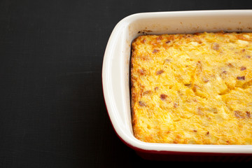 Homemade Cheesy Amish Breakfast Casserole on a black background, low angle view. Space for text.