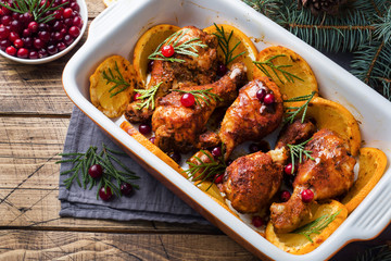 Baked chicken drumstick with oranges and cranberries in a baking sheet on a wooden background. Christmas food Table with decorations.