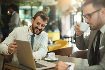 Handsome Smiling Freelancer Showing Finished Project on laptop to a Colleague in Coffee Restaurant