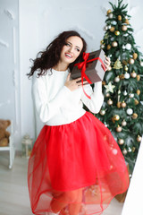 Woman model in a red dress in a photo studio holding a New Year's gift in her hands.
