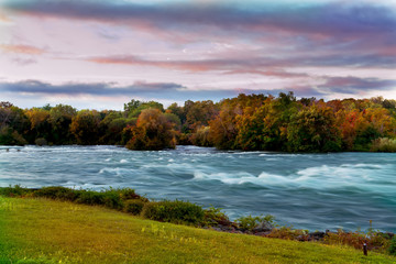 View of the Niagara River in the autumn early morning. Bright colorful trees and a rapid stream of...