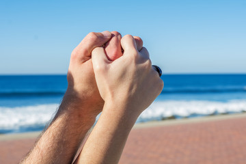 Intertwined hands of a couple in love. With the sea and blue sky in the background.