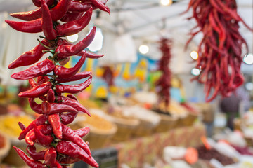 Naklejka premium Fried fruit and spices market, food in baskets with, hand tied chilies hanging in foreground, drying on rope