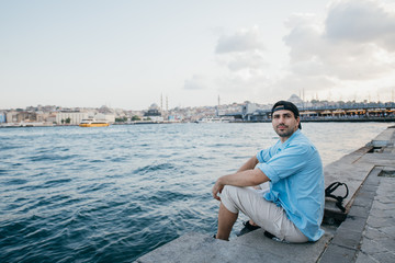 Portrait of a young man against the background of the sea, city, pier and ships.