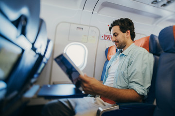 Fototapeta premium The guy flies in an airplane with a magazine in his hands