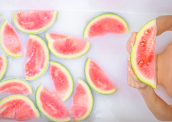 Closeup of woman's hands holding a slice of watermelon. Girl takes a bath with milk and fruit to rejuvenate her skin. Body care.