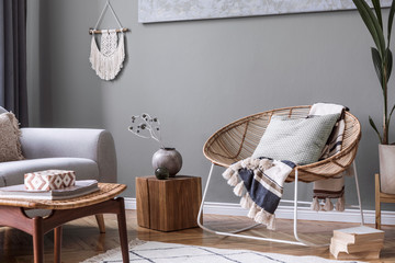 Modern and bohemian composition of interior design at apartment with gray sofa, rattan armchair, cube, plaid, pillows, tropical plants, macrame and elegant accessories. Stylish home decor. Template.