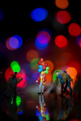 Miniature toy - a man holds colorful balloons among busy commuters crowd with colorful bokeh lights, waiting for someone concept.