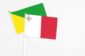 Malta and French Guiana stick flags on white background. High quality fabric, miniature national flag. Peaceful global concept.White floor for copy space.