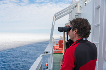 Man with binoculars on the navigational bridge looking