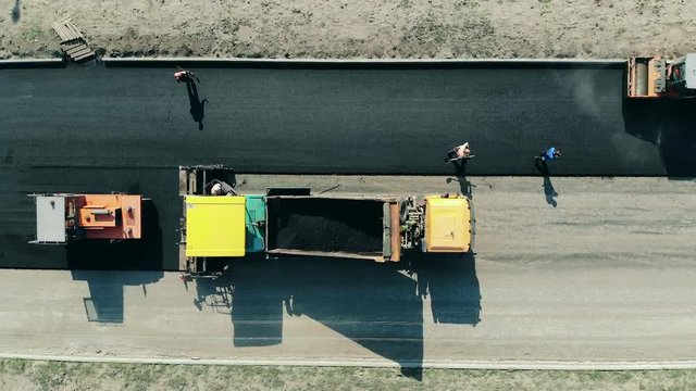 Roadway is getting made from bitum by the workers. Asphalt paver machine on a road construction site.