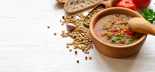 Lentil soup with tomatoes in wooden bowl on white table
