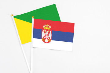 Serbia and French Guiana stick flags on white background. High quality fabric, miniature national flag. Peaceful global concept.White floor for copy space.