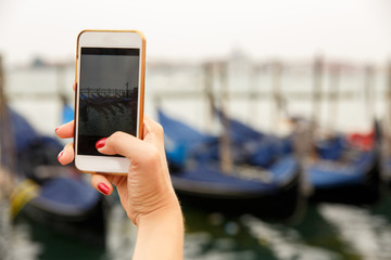 Flooding in Venice. Tourist taking photo on smartphone, gondolas on water in San Marco square, Venice, Italy