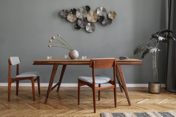 Modern and stylish dining room interior with glamour wooden table , elegant chairs and design decoration. Template. Home decor. Gray background wall. Minimalistic concept of interior design.