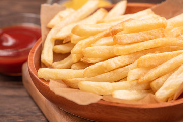 Golden yummy deep French fries on kraft baking sheet paper and serving tray to eat with ketchup and yellow mustard, top view, lifestyle.