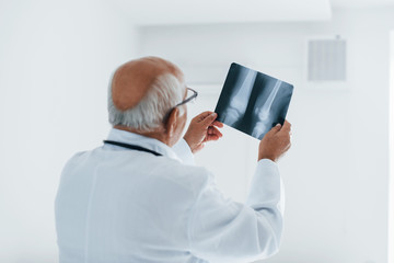 Senior man doctor in white uniform examines x-ray of human legs