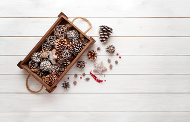 Christmas decorations background. Pine cones in wooden box on white wooden table. Top view, flat lay composition with copy space.