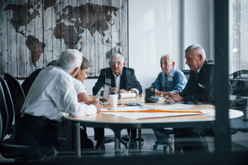 Aged team of elderly businessman architects have a meeting in the office and works with young woman