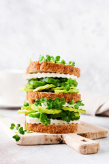 Avocado, cucumber and feta cheese sandwich decorated with micro-greens and multi-grain bread on a simple wooden stand for a healthy breakfast. Selective focus.