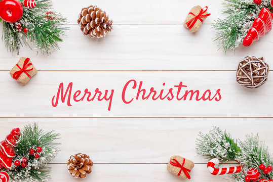 Merry Christmas greeting text on white wooden surface surrounded by Christmas decorations. Top view, flat lay, close-up.