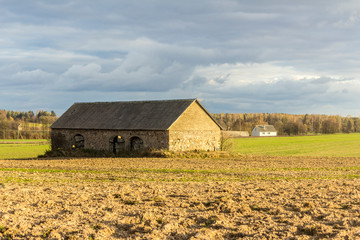 An abandoned stone barn stands in the middle of a plowed field. Industrial dairy farm. Podlasie, Poland.