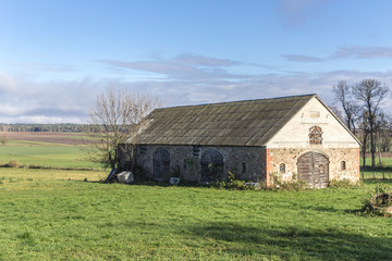 Obraz premium An abandoned stone barn stands in a green meadow. Industrial dairy farm. Podlasie, Poland.