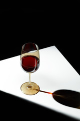 Object shot of a golden wineglass, staying on a white table. The light falls on the glass, the glass casts a shadow. The glass is half full of wine.
