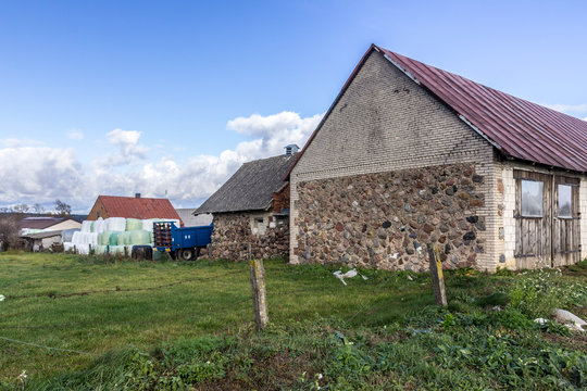 Old stone barns, agricultural machinery, a silo bale pyramid, green meadow. Industrial dairy farm. Podlasie, Poland.