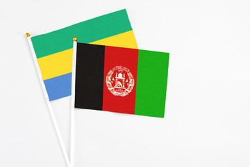 Fototapeta premium Afghanistan and Gabon stick flags on white background. High quality fabric, miniature national flag. Peaceful global concept.White floor for copy space.
