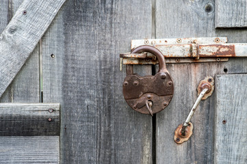 An ancient closed wrought-iron lock with an inserted key hangs on the bolt of an old wooden door. Background