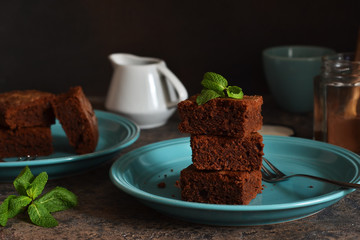 Chocolate brownie - a classic American dessert in a blue plate on a concrete background.