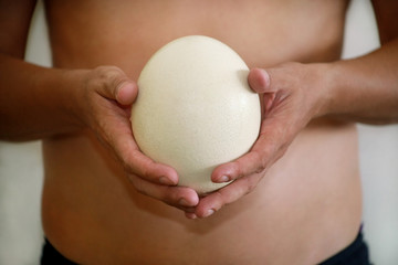 Male hands holding of big ostrich egg on white background, size comparison, close up. Organic fresh egg. Healthy food. Ostrich egg as symbol of birth. Huge white egg shell of african ostrich.