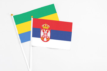 Serbia and Gabon stick flags on white background. High quality fabric, miniature national flag. Peaceful global concept.White floor for copy space.