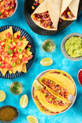 Mexican foodflatlay, overhead shot on a turquoise background. Nachos, tequila with limes, taco shells, burritos, guacamole