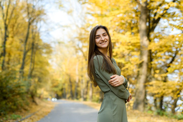 Portrait of brunette woman in green dress posing in autumn park