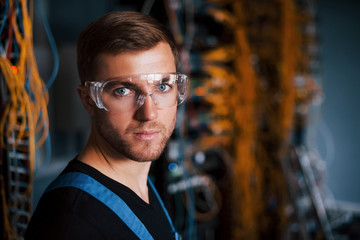 Young man in uniform works with internet equipment and wires in server room