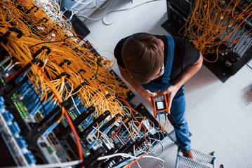 Top view of young man in uniform with measuring device that works with internet equipment and wires...