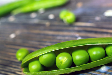 an open pod of green peas lies on a wooden table close up