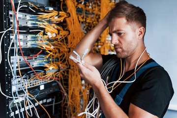Young man in uniform feels confused and looking for a solution with internet equipment and wires in...