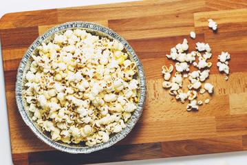 Popcorn in foil plate on wooden background. Homemade Corn Grain Cooking