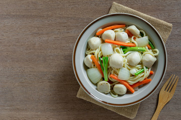 top view of stir fried japanese noodles with fish ball and vegetables in a ceramic dish on wooden table. asian homemade style food concept.