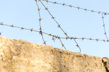 barbed wire with spikes over a concrete fence in the background of blue sky