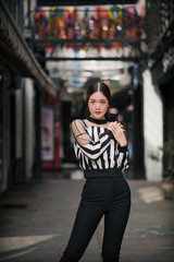 Fototapeta premium street portrait, strong woman in black, confident woman, lady in city, portrait of Asian female, half body ,posing her hands on one shoulder wearing stripe top