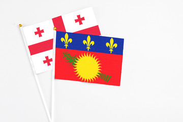Guadeloupe and Georgia stick flags on white background. High quality fabric, miniature national flag. Peaceful global concept.White floor for copy space.