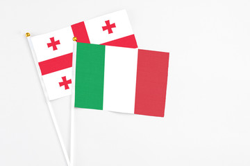 Italy and Georgia stick flags on white background. High quality fabric, miniature national flag. Peaceful global concept.White floor for copy space.