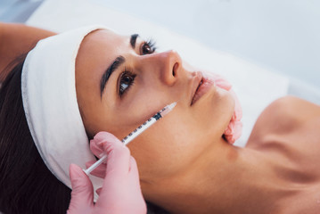 Close up view of woman that lying down in spa salon and have injection by the syringe into her face skin
