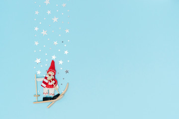 Christmas toy Snowman skier in red suit with starry silver confetti in form of snow falling from above on blue backdrop. Happy New Year 2020 concept design flat lay. Copy space, for blog, advertising