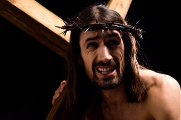 jesus holding heavy wooden cross isolated on black