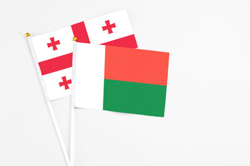 Madagascar and Georgia stick flags on white background. High quality fabric, miniature national flag. Peaceful global concept.White floor for copy space.